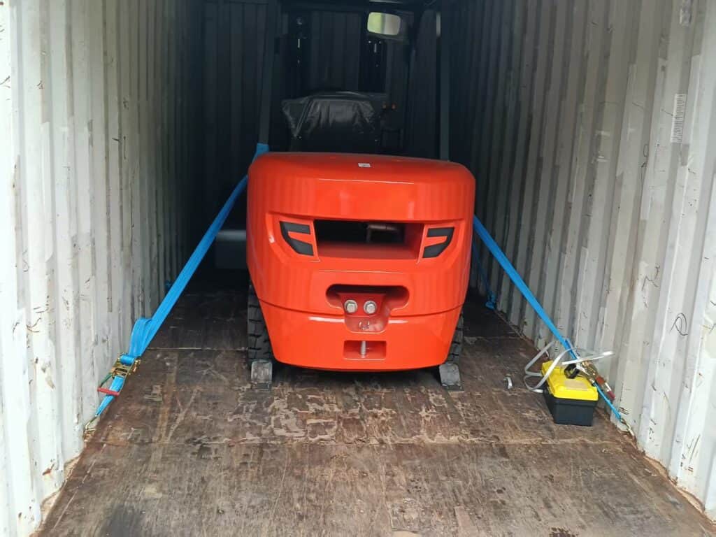 Carretilla elevadora sujeta dentro de un contenedor con correas azules y calzos en las ruedas